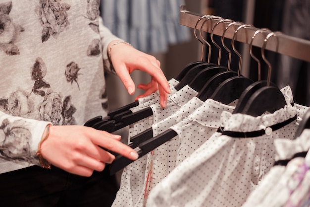 Mujer manos en perchas en una tienda comprando ropa