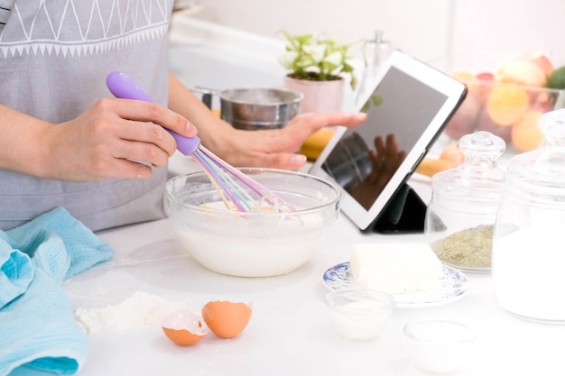 Mujer de manos de primer plano parada en la cocina y cocinando la masa Mirando la tableta
