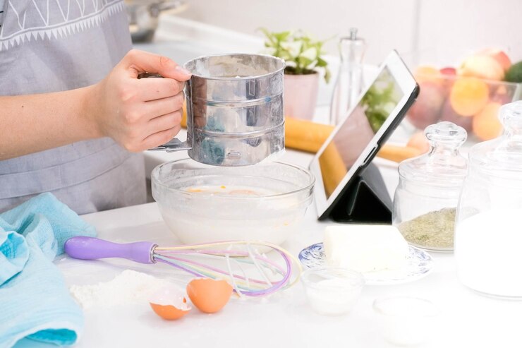 Foto mujer de manos de primer plano parada en la cocina y cocinando la masa mirando la tableta