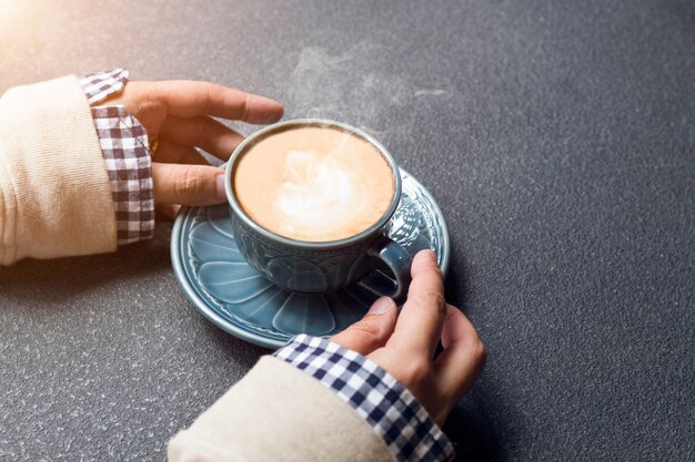 La mujer de las manos que sostienen la taza de café caliente cerca de la luz de la mañana de la ventana.