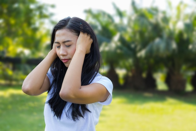 Mujer manos sobre su cabeza y siente dolor de cabeza mientras camina en el parque