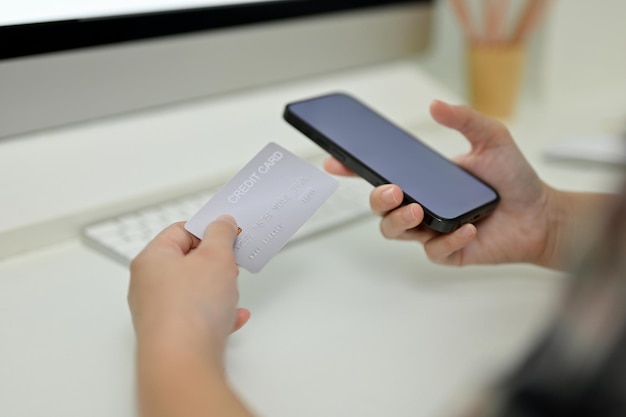 Una mujer manos sosteniendo un teléfono inteligente y una tarjeta de crédito sobre su escritorio