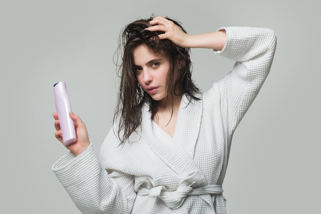 Mujer mantenga botella de champú y acondicionador. Mujer joven aplicando mascarilla para el cabello, después de la ducha. Hermosa mujer caucásica con botella de bálsamo posando con el pelo mojado.