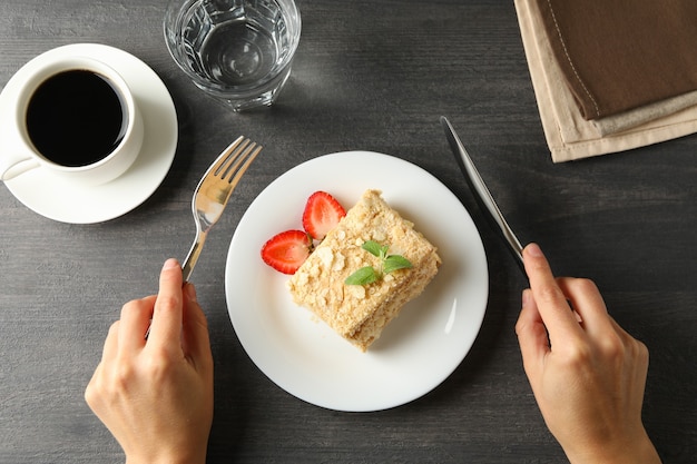 Mujer mantenga cubiertos sobre mesa negra con plato de pastel de Napoleón, vista superior