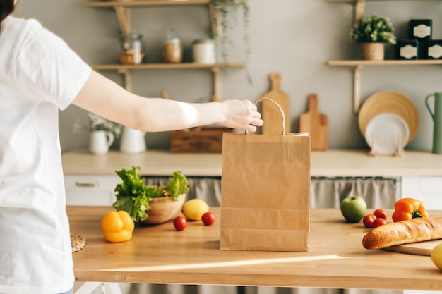 Mujer mantenga eco bolsa de compras con verduras frescas y baguette en cocina moderna