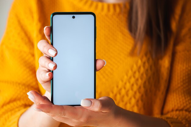 Mujer mantenga maqueta de pantalla de teléfono móvil en manos en suéter naranja