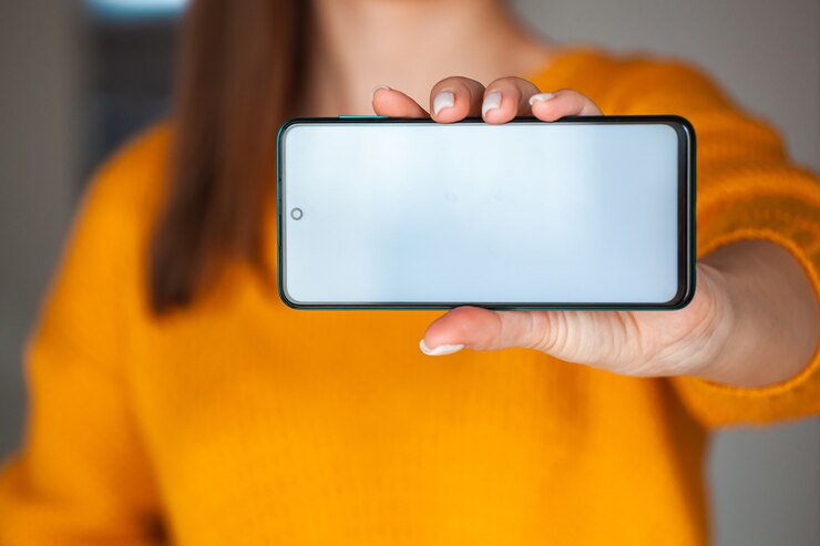 Foto mujer mantenga la pantalla del teléfono móvil en las manos en suéter naranja