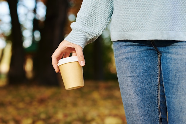 Mujer mantenga una taza de café para llevar en el parque otoño