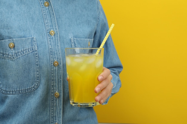 Mujer mantenga vaso de refresco en superficie amarilla