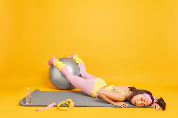 La mujer mantiene las manos en la pelota de fitness se siente muy cansada después de un entrenamiento cansado vestida con ropa deportiva se encuentra en karemat