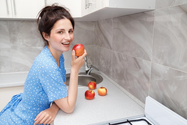 Una mujer con una manzana en la cocina comiendo sano