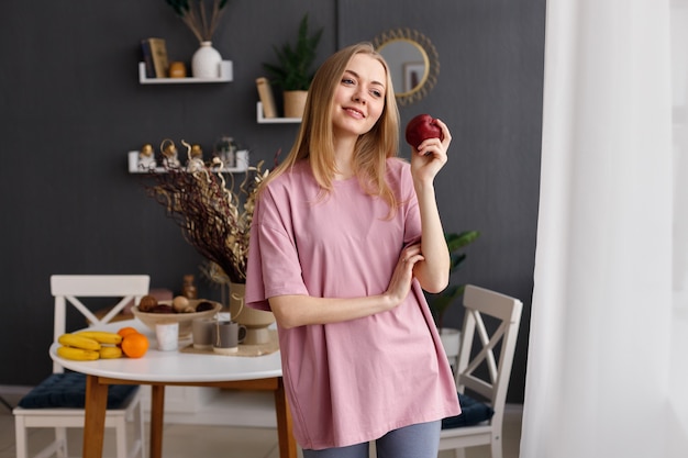 Mujer con manzana roja en casa sonriendo