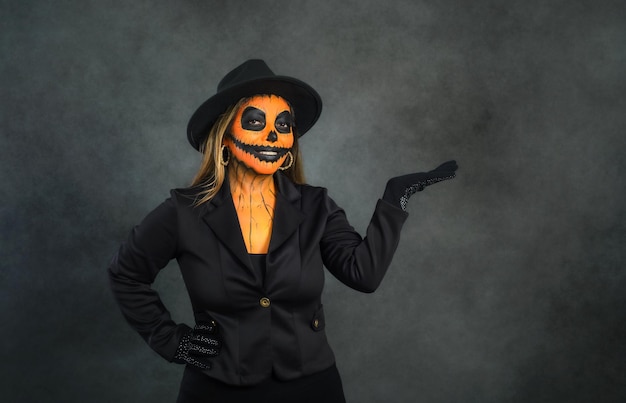 Mujer maquillada como una calabaza para celebrar Halloween fingiendo tener algo en la mano. Fondo oscuro con espacio de copia.