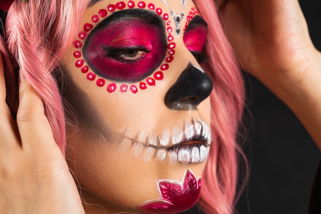 Mujer con maquillaje de calavera de azúcar y cabello rosado aislado sobre fondo negro. Dia de los Muertos. Víspera de Todos los Santos. Copie el espacio.