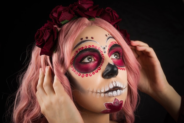 Mujer con maquillaje de calavera de azúcar y cabello rosado aislado sobre fondo negro