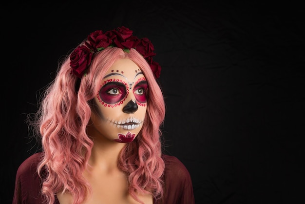 Mujer con maquillaje de calavera de azúcar y cabello rosado aislado sobre fondo negro
