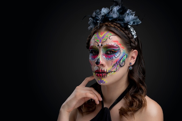 Mujer con maquillaje de catrina tradicional por dia de muertos y usando un vestido negro con fondo