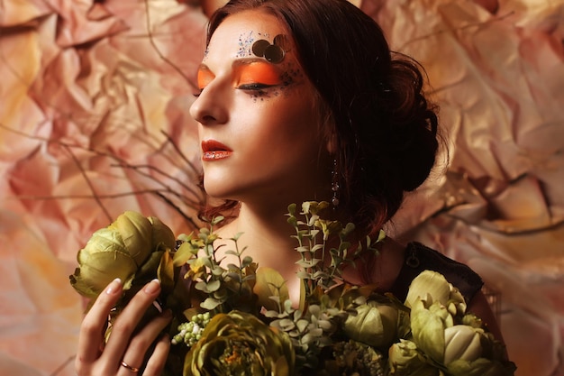 Mujer con maquillaje creativo brillante sosteniendo flores verdes
