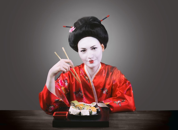 Mujer en maquillaje de geisha comiendo sushi fondo gris