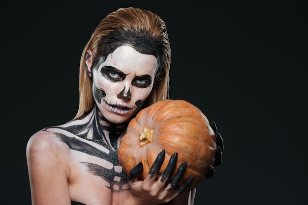 Mujer con maquillaje de halloween esqueleto sosteniendo calabaza sobre fondo negro