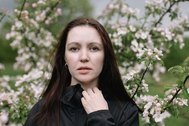 Mujer con maquillaje natural cosmética floral para la piel de la cara chica posando en ramas de flores de manzano floreciente en primavera