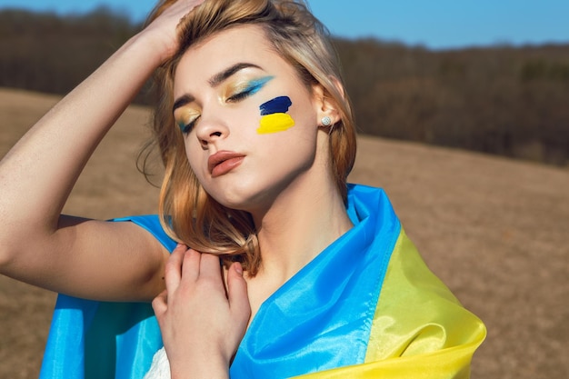 Mujer con maquillaje patriótico envuelto en soporte de bandera ucraniana con concepto de Ucrania