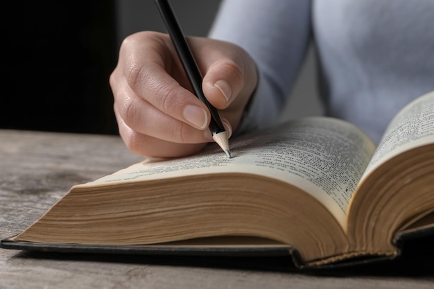 Mujer marcando en la Biblia en el primer plano de la mesa de madera
