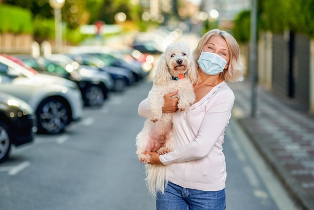 Mujer una máscara antivirus con un perro en una calle de la ciudad.