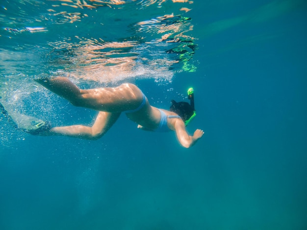 Mujer con máscara de buceo y aletas mirando el fondo del mar