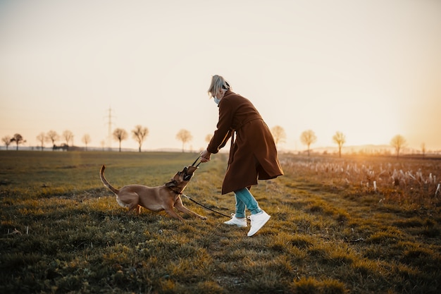 Mujer con máscara camina sola con un perro al aire libre debido a la cuarentena de corona