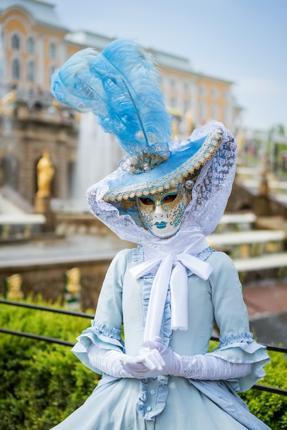 Mujer con una máscara de carnaval y un vestido azul con el telón de fondo de las fuentes en un día soleado