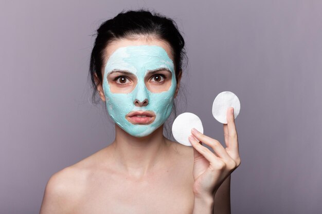 mujer con una máscara cosmética en la cara y almohadillas de algodón en las manos