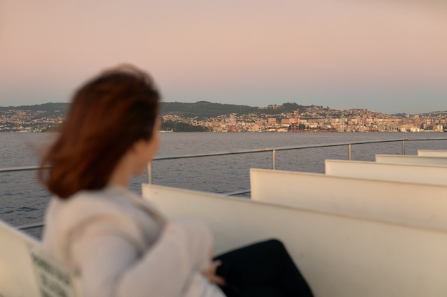 Mujer con máscara y gafas de sol en un barco de cercanías al atardecer.