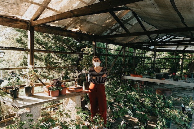 Una mujer con una máscara haciendo jardinería durante una súper puesta de sol, con muchas plantas y flores a su alrededor, con espacio de copia