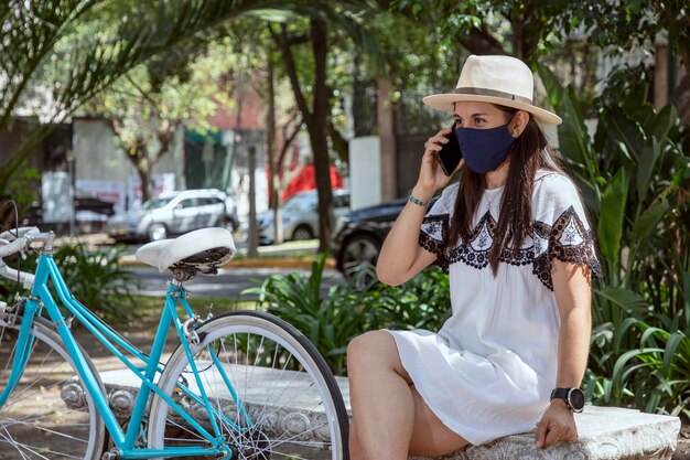 Mujer con máscara haciendo una llamada de teléfono celular en el parque