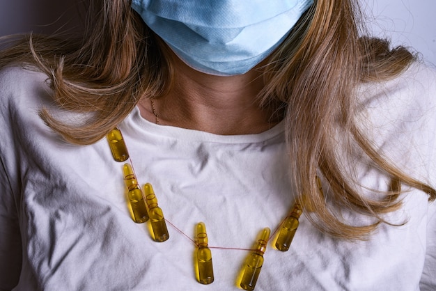 Mujer con máscara médica y camiseta blanca. Mujer vistiendo joyas de ampollas médicas