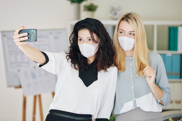 Mujer en máscara médica fotografiando con colega