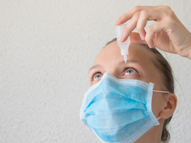 Mujer en una máscara médica con gotas para los ojos. Prevención de infecciones virales.