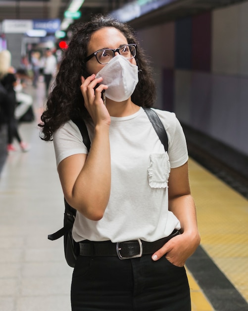 Mujer con máscara médica hablando por teléfono mientras espera el metro