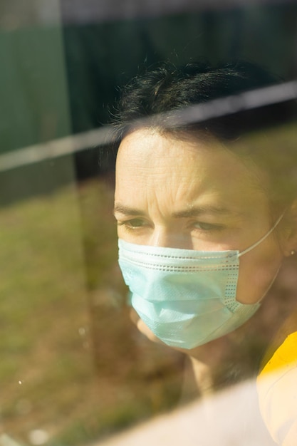 La mujer con una máscara médica mira por la ventana.