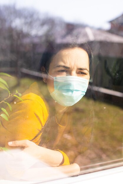 La mujer con una máscara médica mira por la ventana.