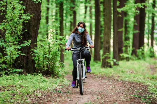 Mujer con máscara médica monta una bicicleta en el parque