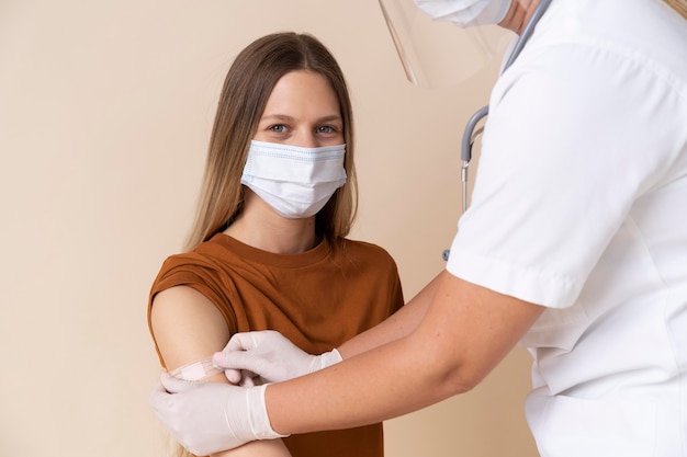 Foto mujer con máscara médica obteniendo una pegatina en el brazo después de recibir una vacuna