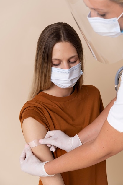 Foto mujer con máscara médica obteniendo una pegatina en el brazo después de recibir una vacuna