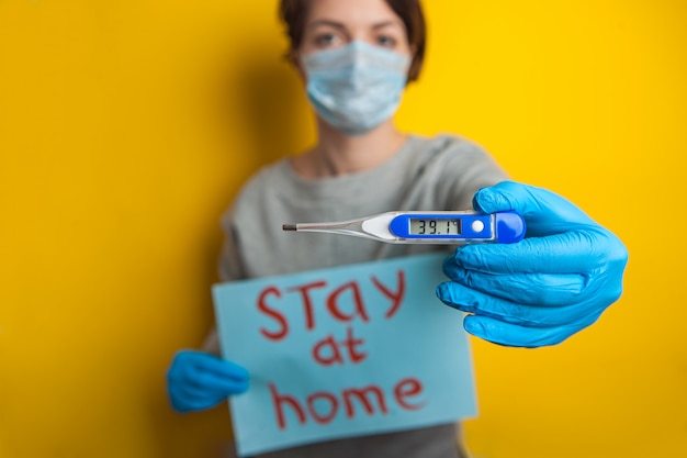 Foto mujer en una máscara médica con una temperatura. sosteniendo un termómetro en sus manos. condición leve de un paciente con coronavirus. quedarse en casa