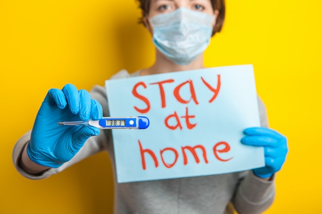 Foto mujer en una máscara médica con una temperatura. sosteniendo un termómetro en sus manos. condición leve de un paciente con coronavirus. quédese en casa hasta que llegue el médico. distribución de covid-19