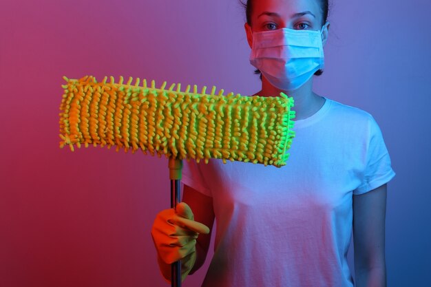 Mujer con una máscara médica tiene una fregona. Gradiente de neón luz azul roja