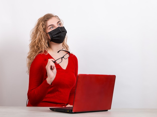 Mujer en una máscara médica, trabajando remotamente en la computadora en blanco.