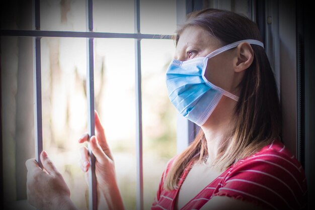 Mujer con máscara mirando por la ventana