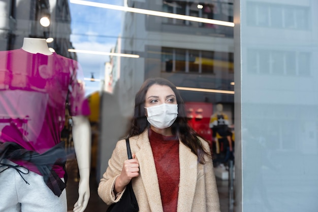 Foto mujer con máscara de pie junto a la tienda de ropa